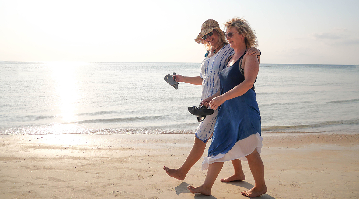 Two women walking and laughing along the coast line on a sunny day with the sea in the background